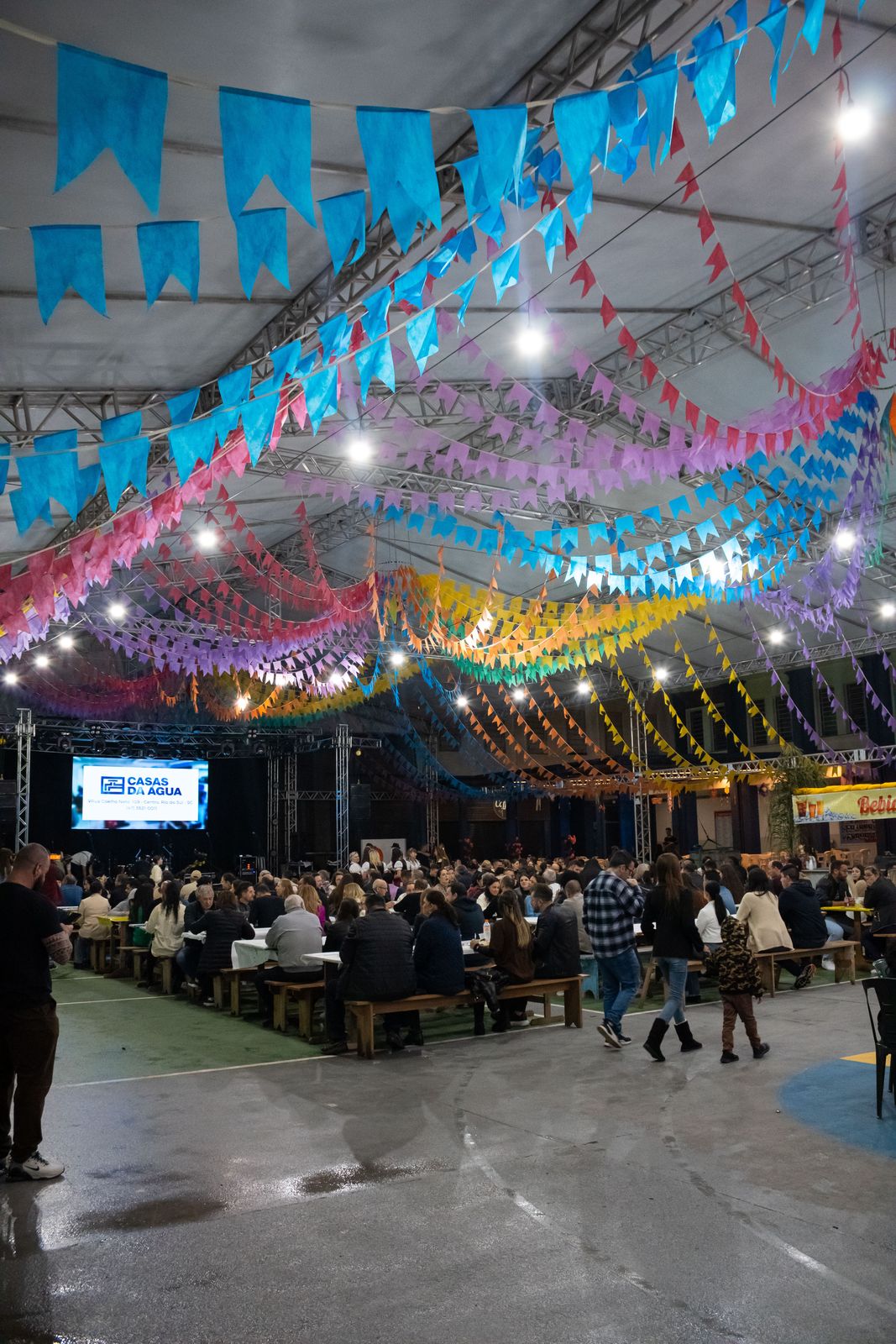 Salão da festa lotado de fiéis sob as bandeirinhas coloridas